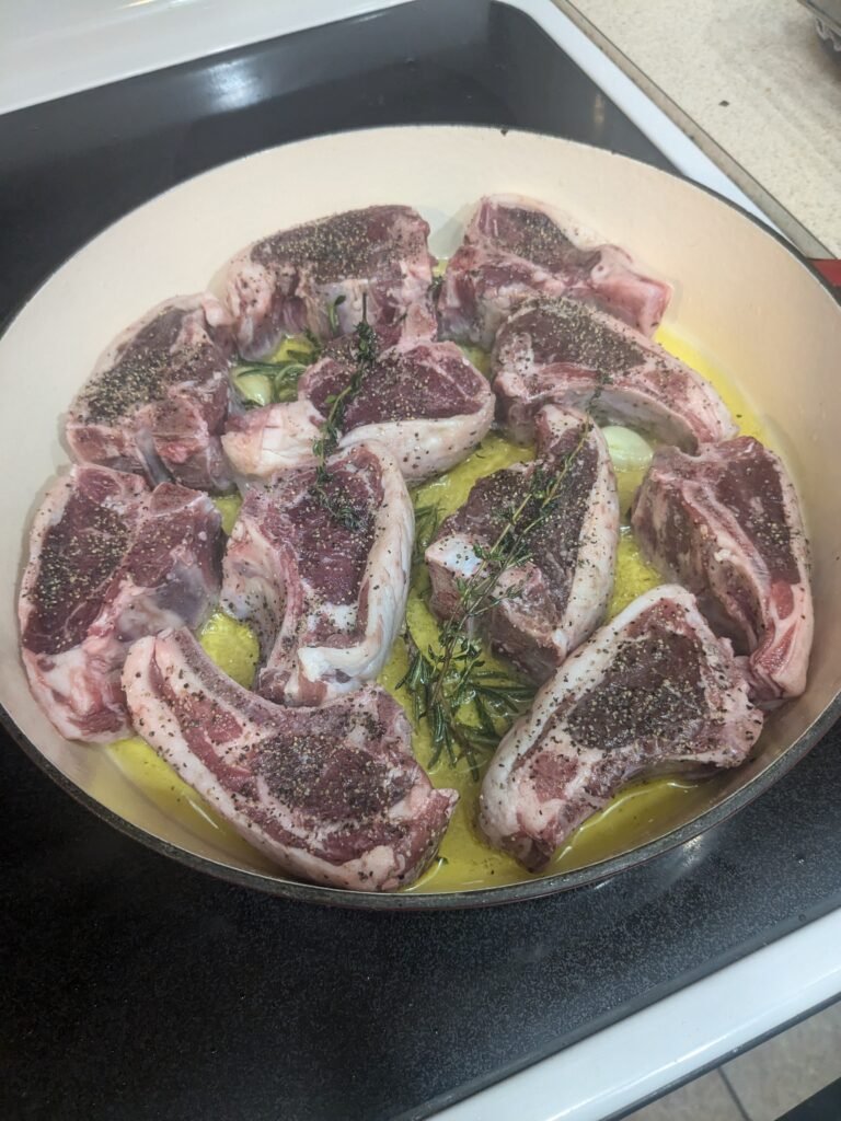 Seared lamb chops in a hot cast iron pan with garlic, rosemary, and lemon