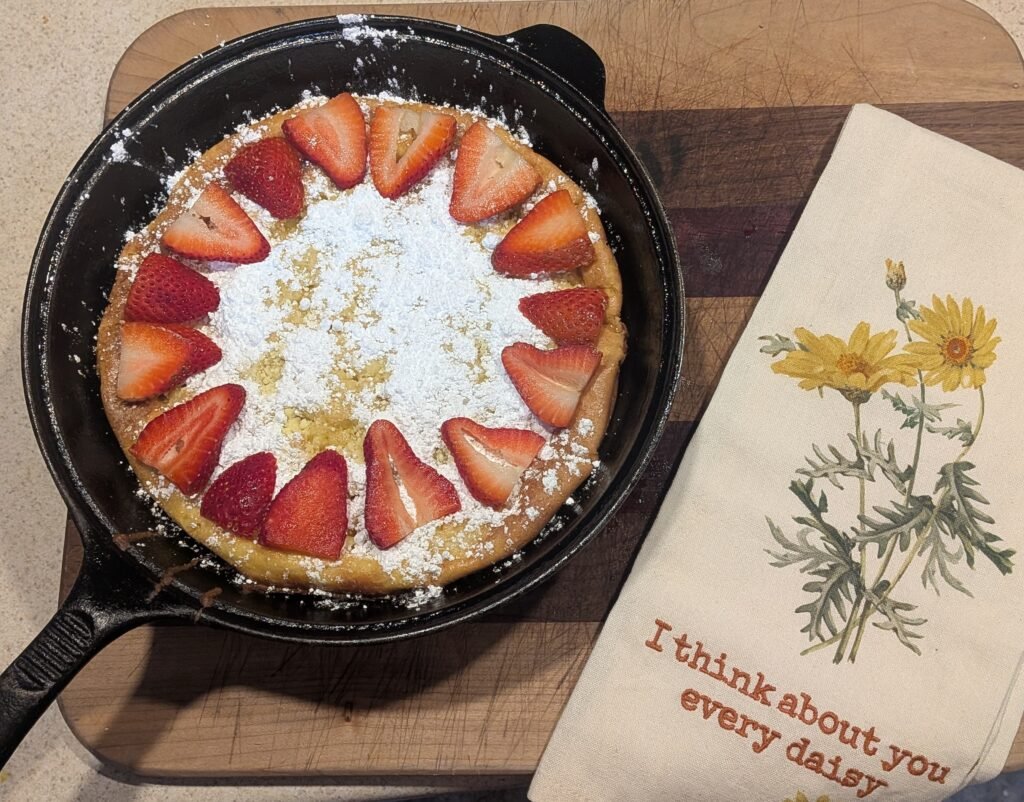 Homemade sourdough Dutch baby pancake in a cast-iron pan. Topped with powdered sugar and fresh picked strawberries.