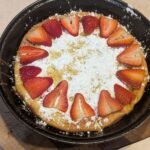 Homemade sourdough Dutch baby pancake topped with powdered sugar and fresh strawberries