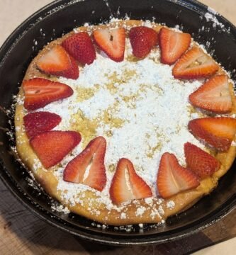 Homemade sourdough Dutch baby pancake topped with powdered sugar and fresh strawberries