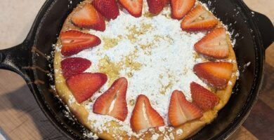 Homemade sourdough Dutch baby pancake topped with powdered sugar and fresh strawberries