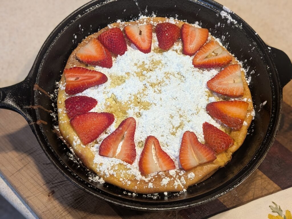 cast iron skillet with sourdough dutch baby pancake and sprinkled with powdered sugar and strawberries.