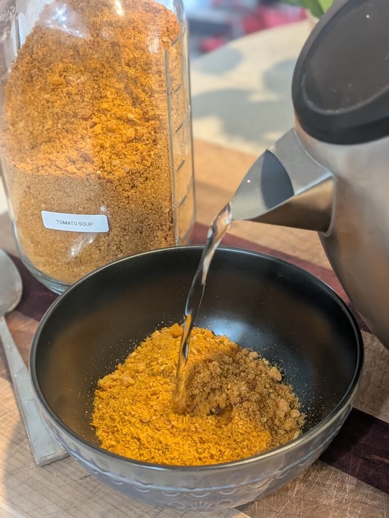 An instant kettle of hot water being poured into a bowl of freeze dried tomato soup