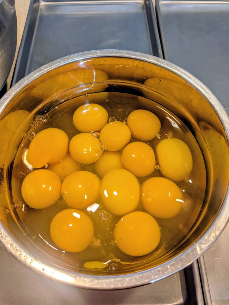 A dozen and a half farm-fresh eggs cracked into a large stainless steel bowl