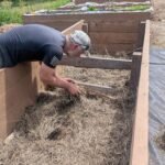 Filling and preparing a raised garden bed with logs and hay before filling with soil.