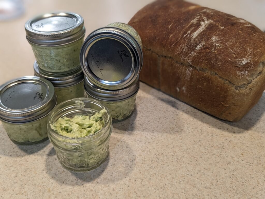 Jars of garlic scape butter paired with a fresh loaf of sourdough bread.